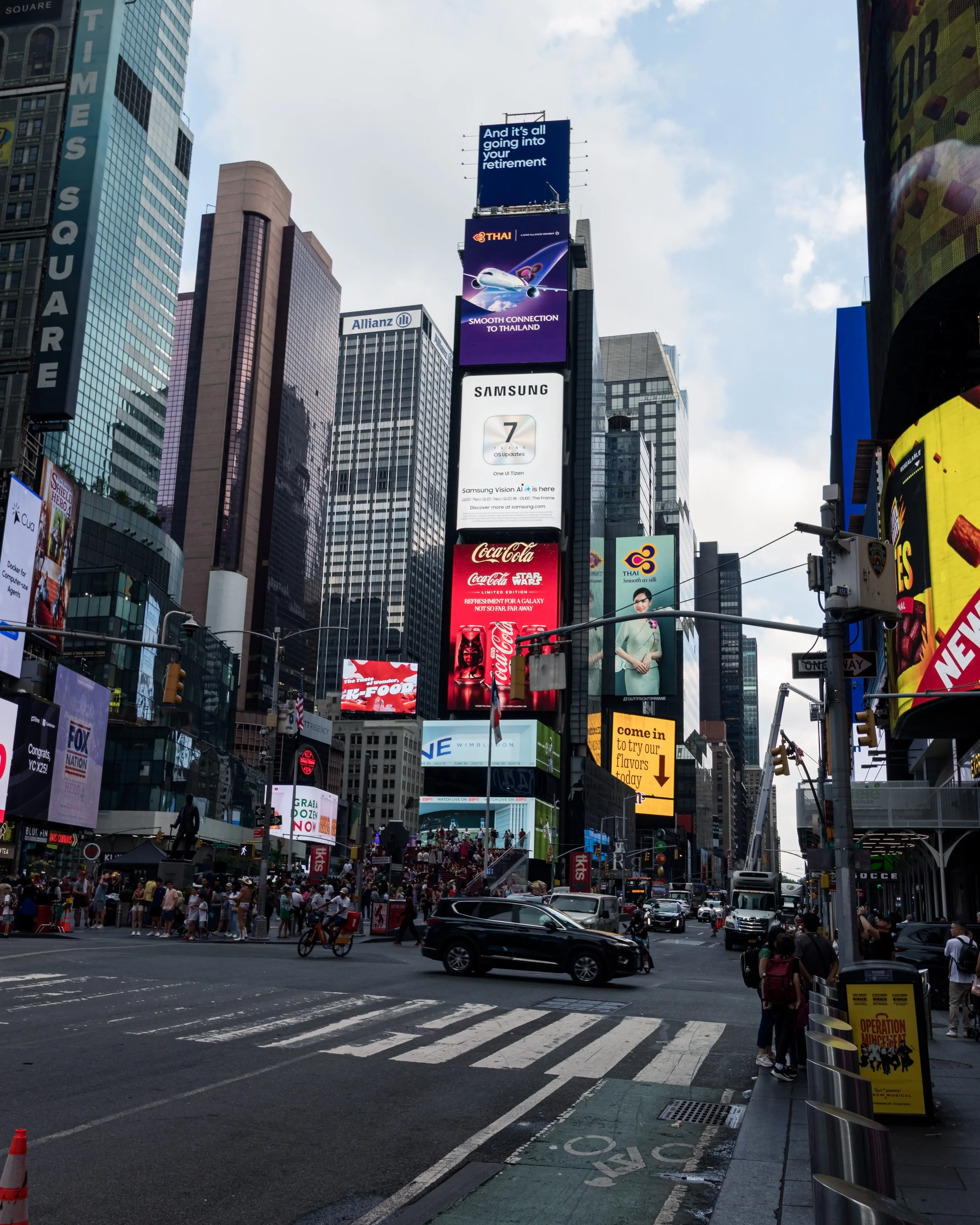 Tall buildings and illuminated billboards crowd a busy city intersection.