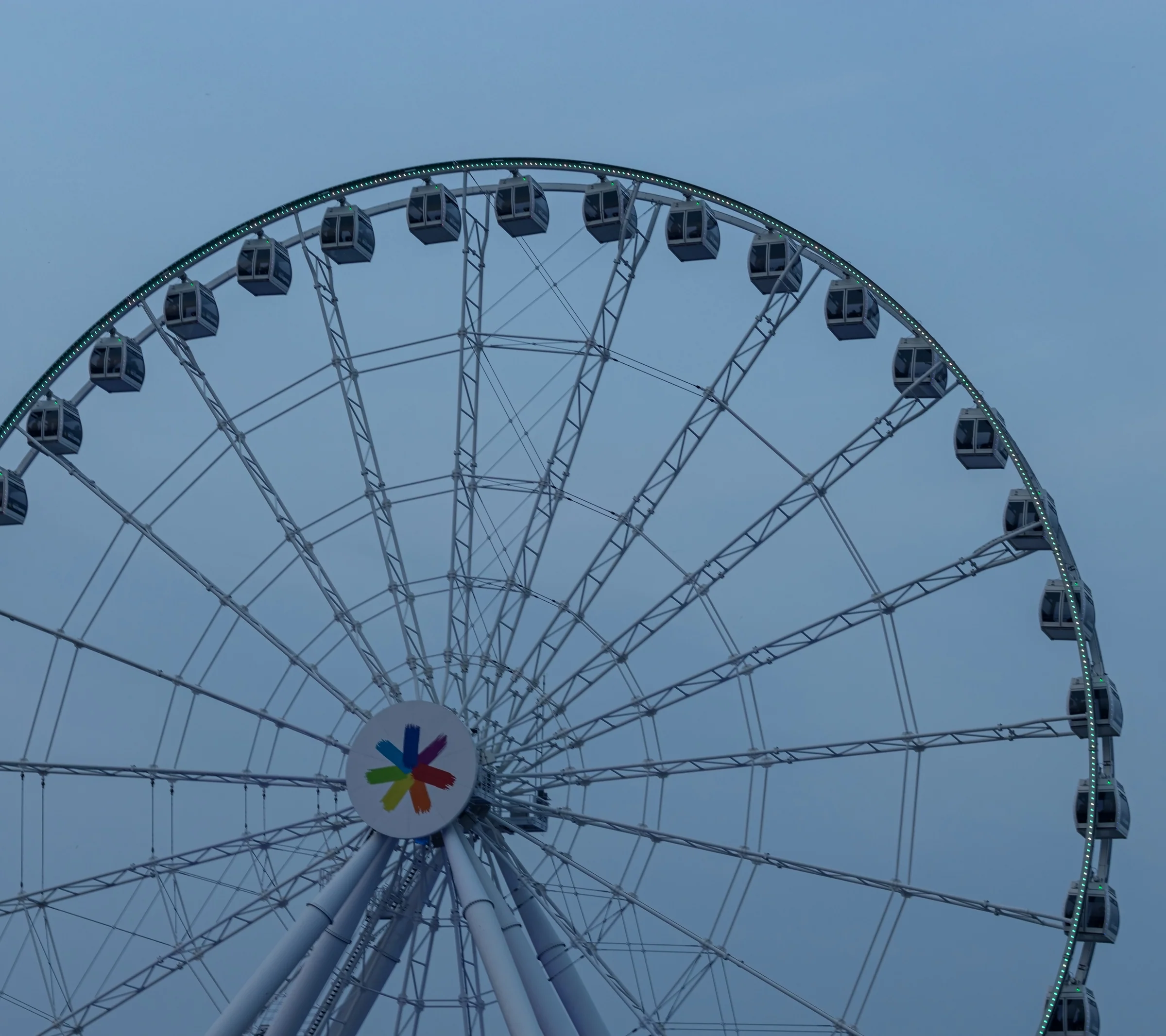 The upper arc of an observation wheel rises against a pale blue-grey sky.