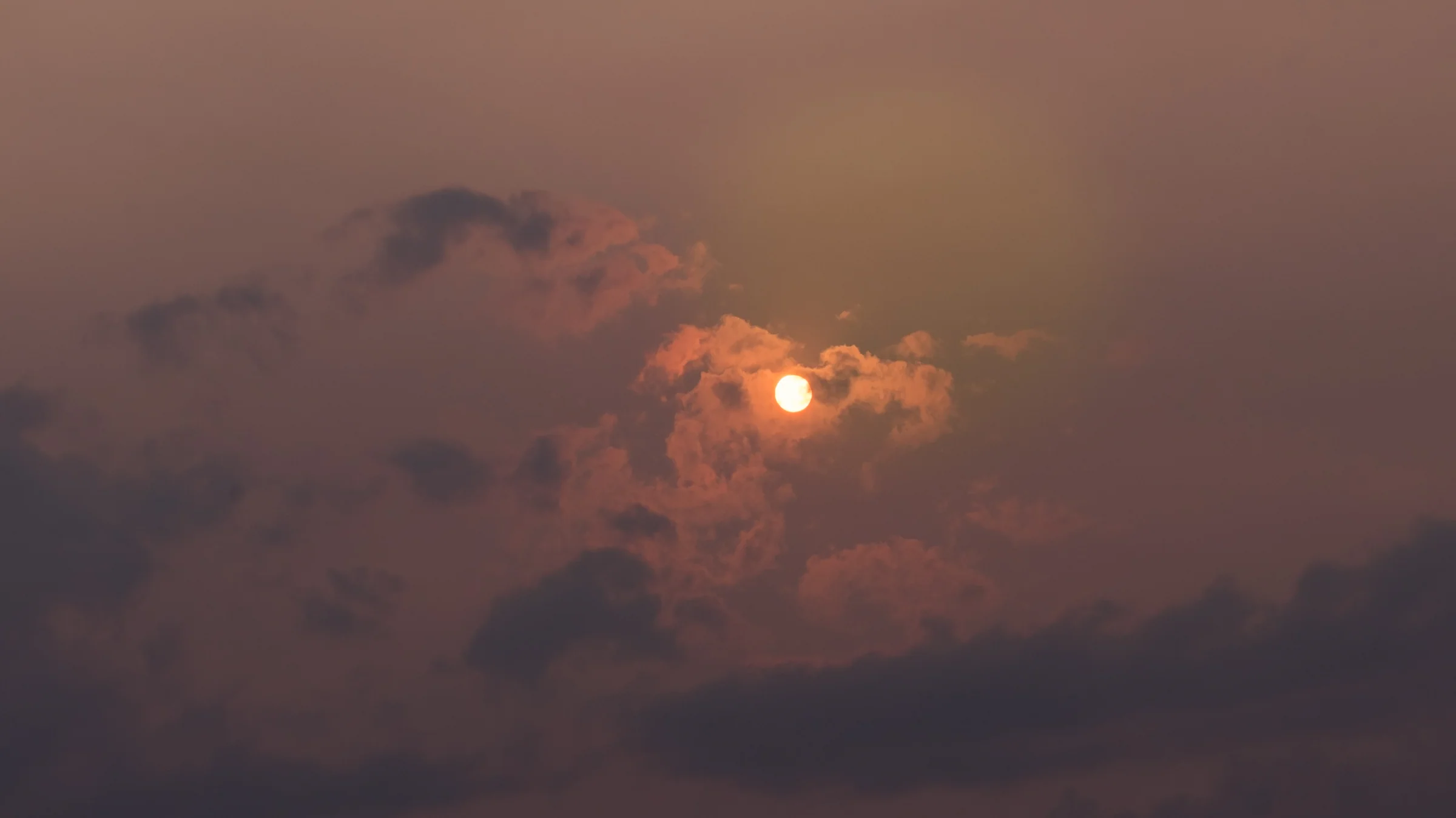 A muted orange sun glows through layers of smoky-looking cloud.