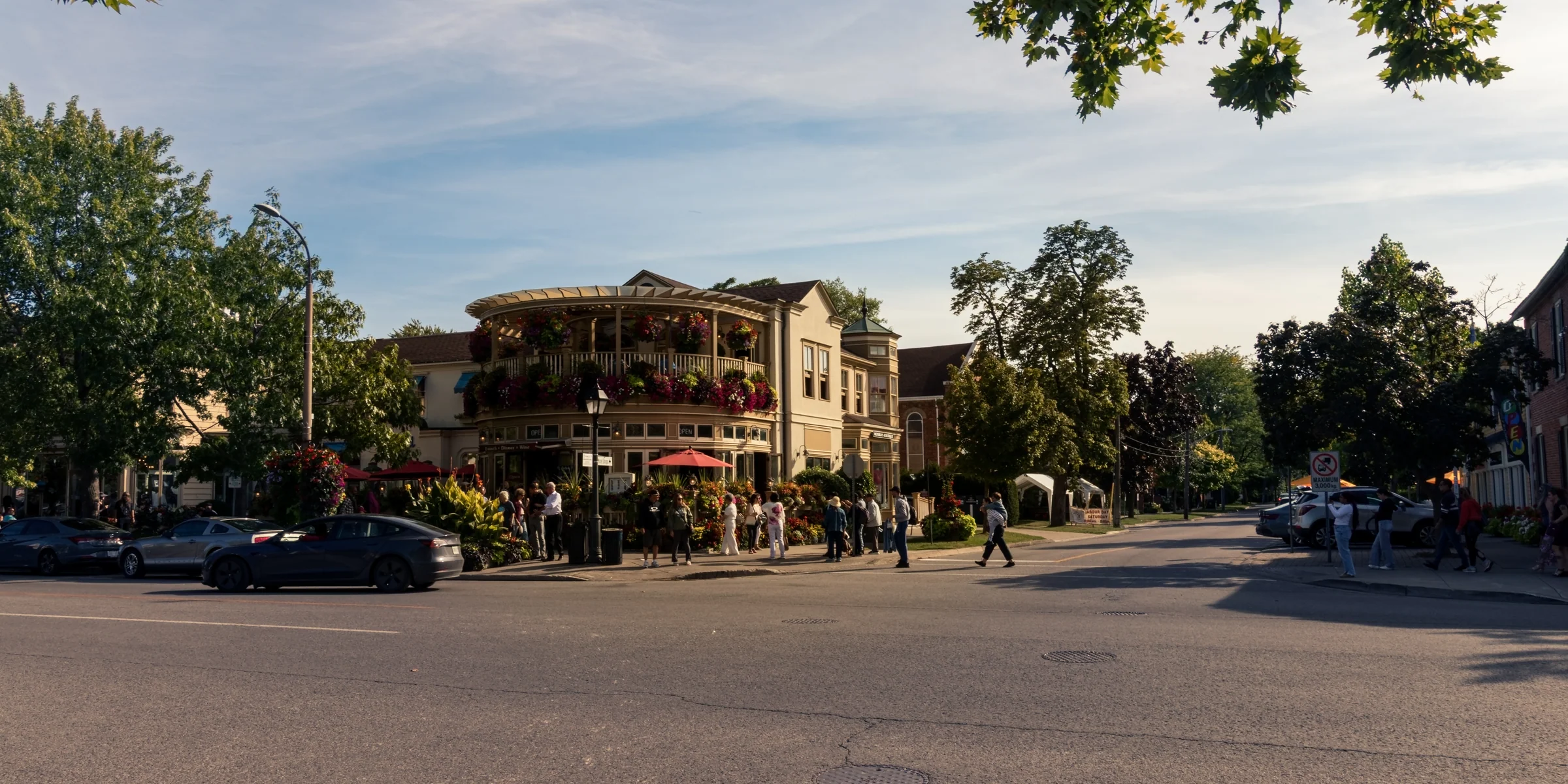 A broad street corner opens onto a historic building with balconies and leafy trees.