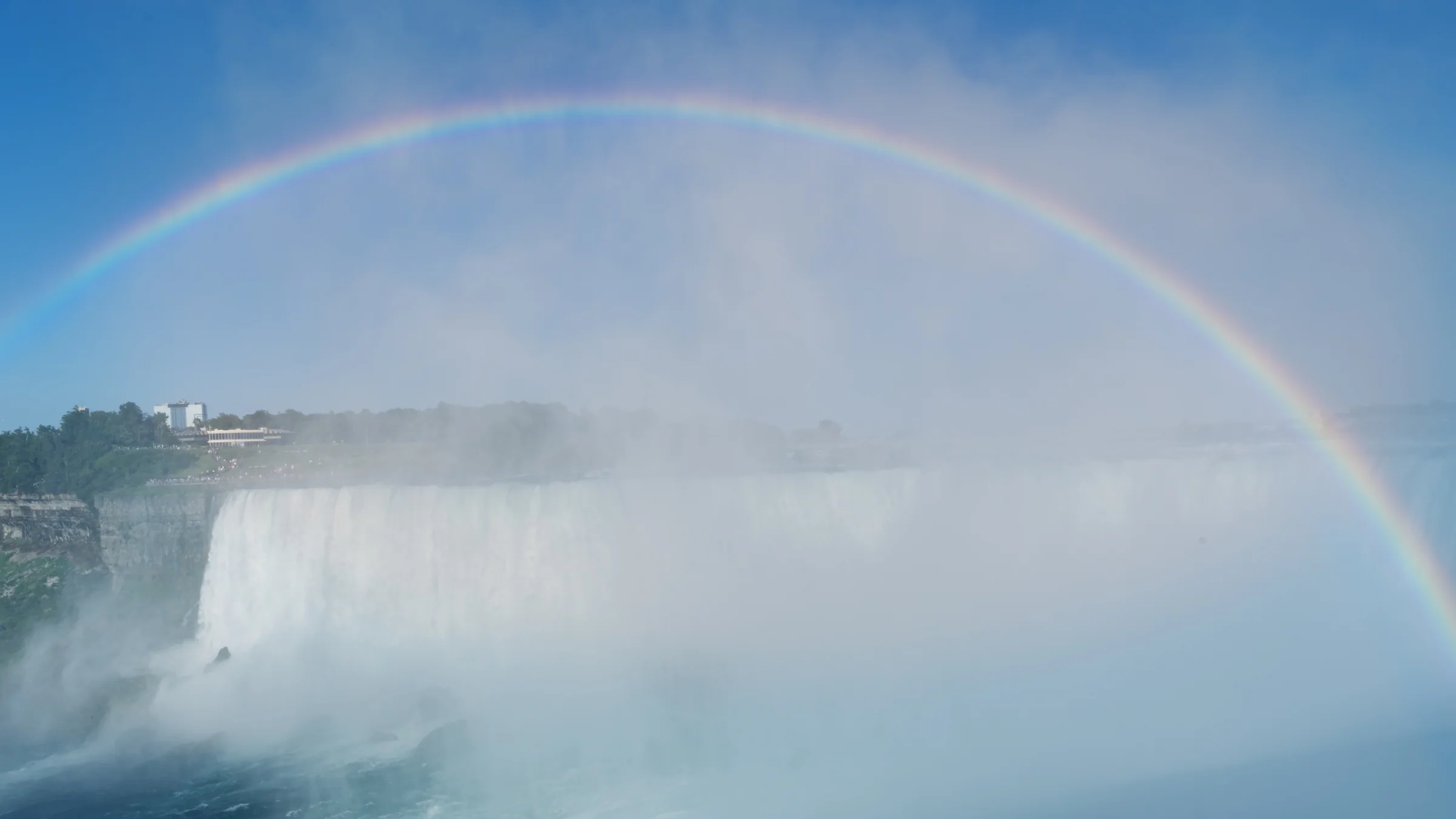 A broad rainbow curves over a waterfall partly hidden by billowing white mist.