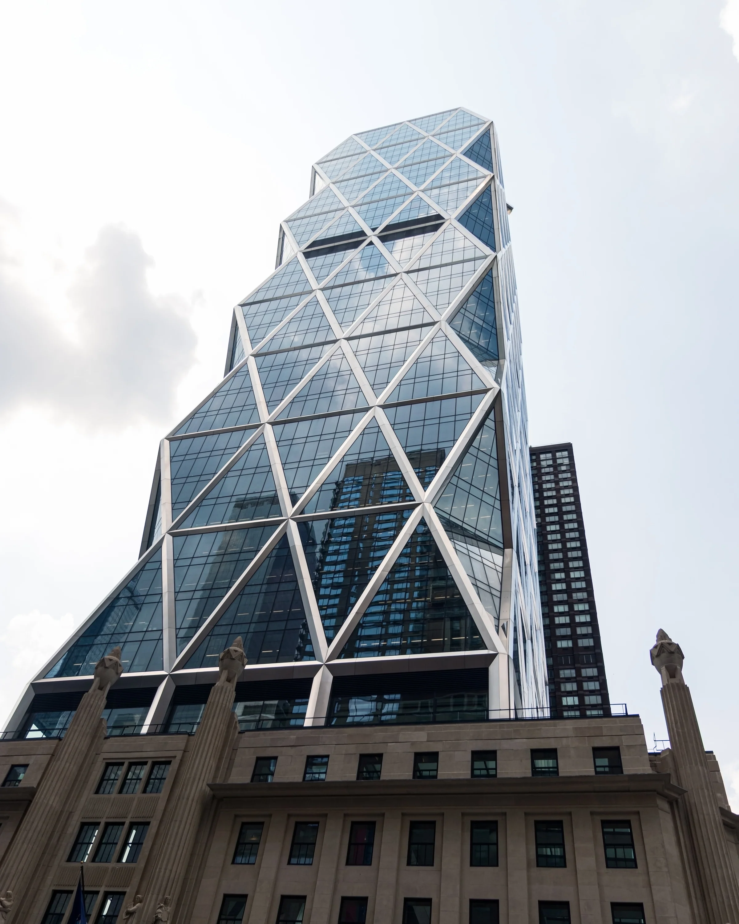 A faceted glass tower rises above a traditional stone building beneath bright cloud.