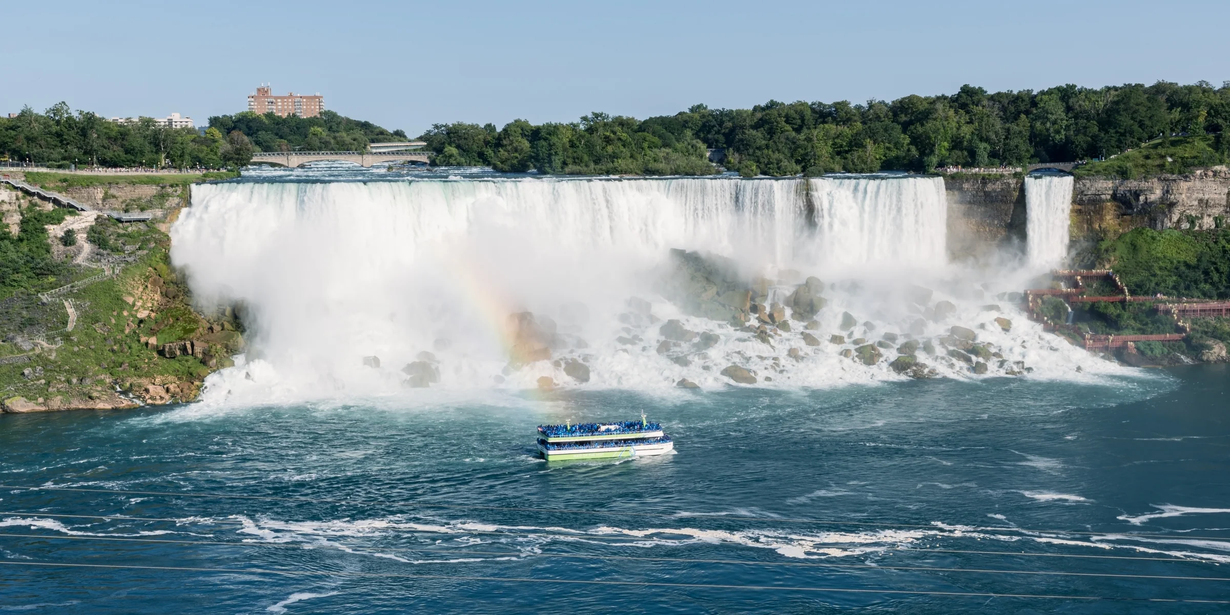 A sightseeing boat passes beneath a wide curtain of falling water and drifting mist.