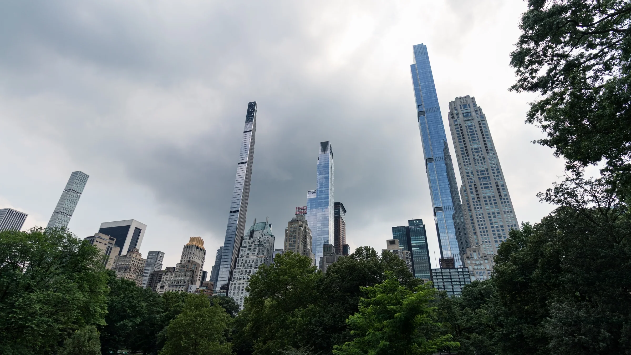 A cluster of slender skyscrapers rises beyond the leafy edge of an urban park.