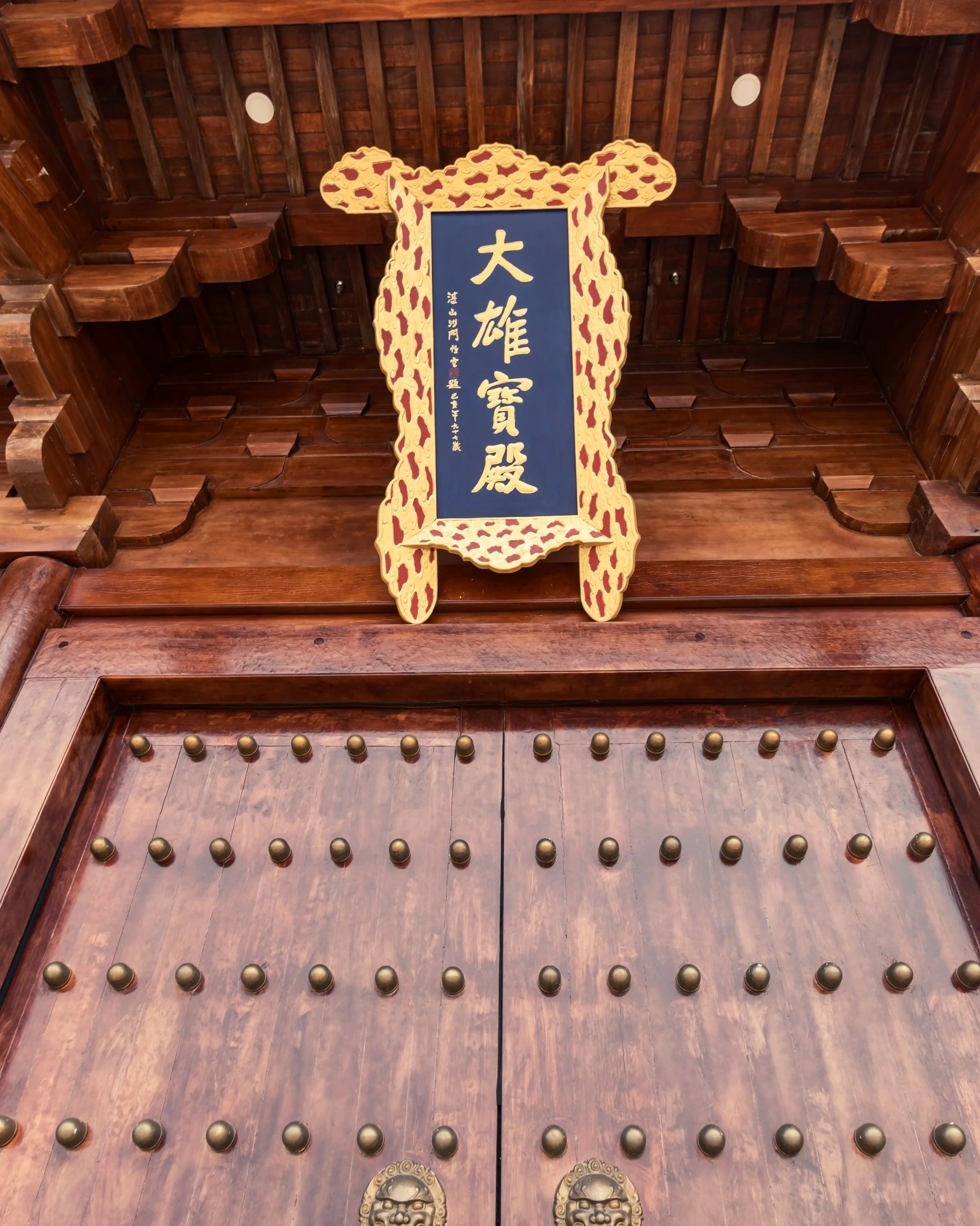 An ornate wooden doorway is framed by carved beams and a hanging blue-and-gold plaque.