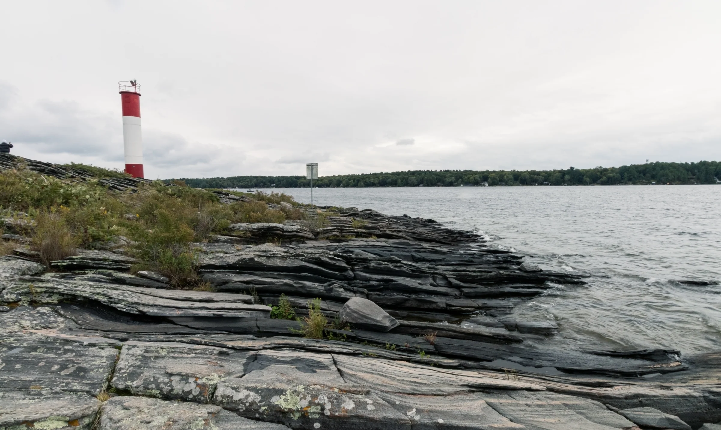 A red-and-white lighthouse rises from a rocky shoreline beneath an overcast sky.