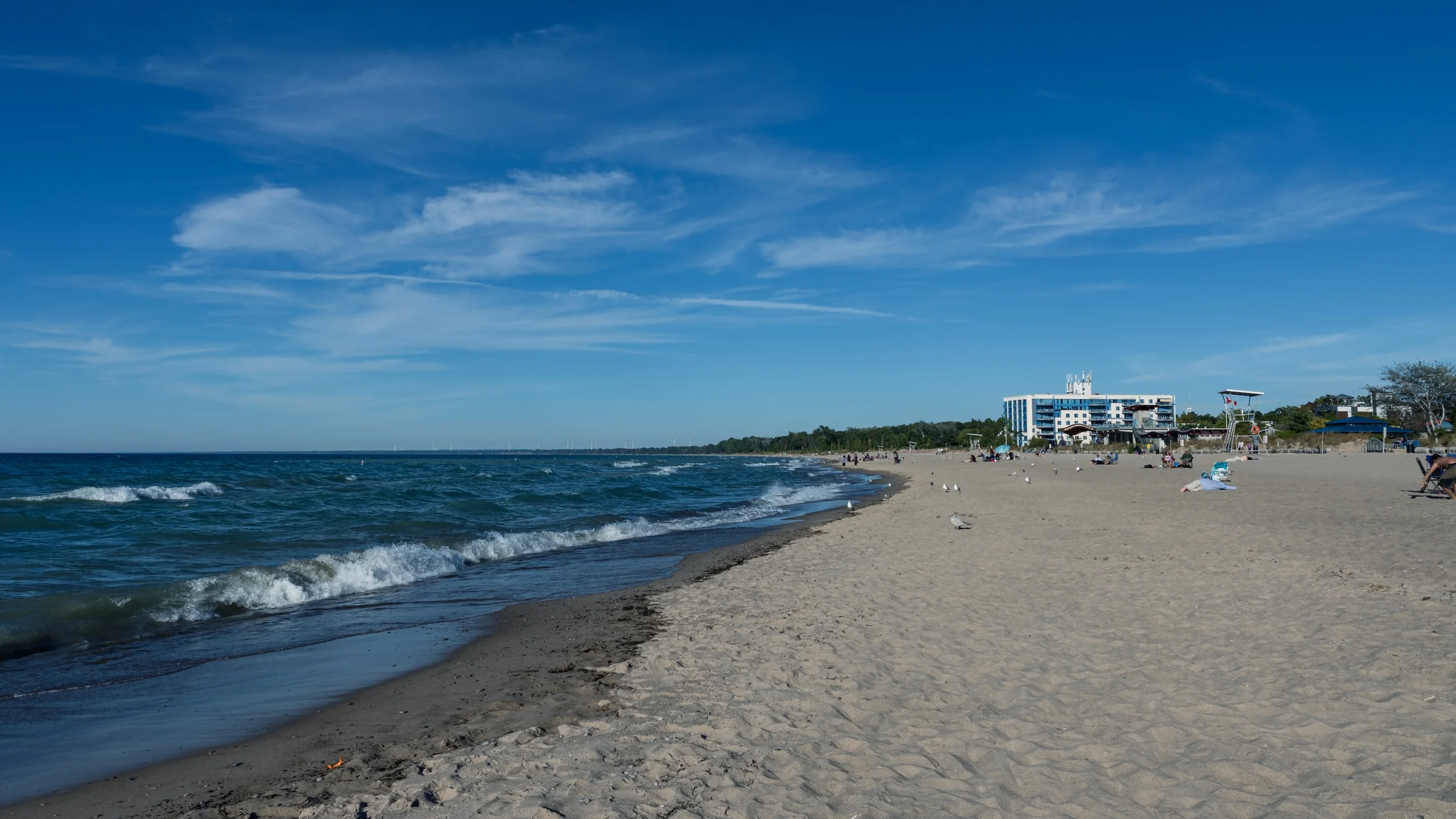 A gently curving beach meets blue water beneath wispy clouds.