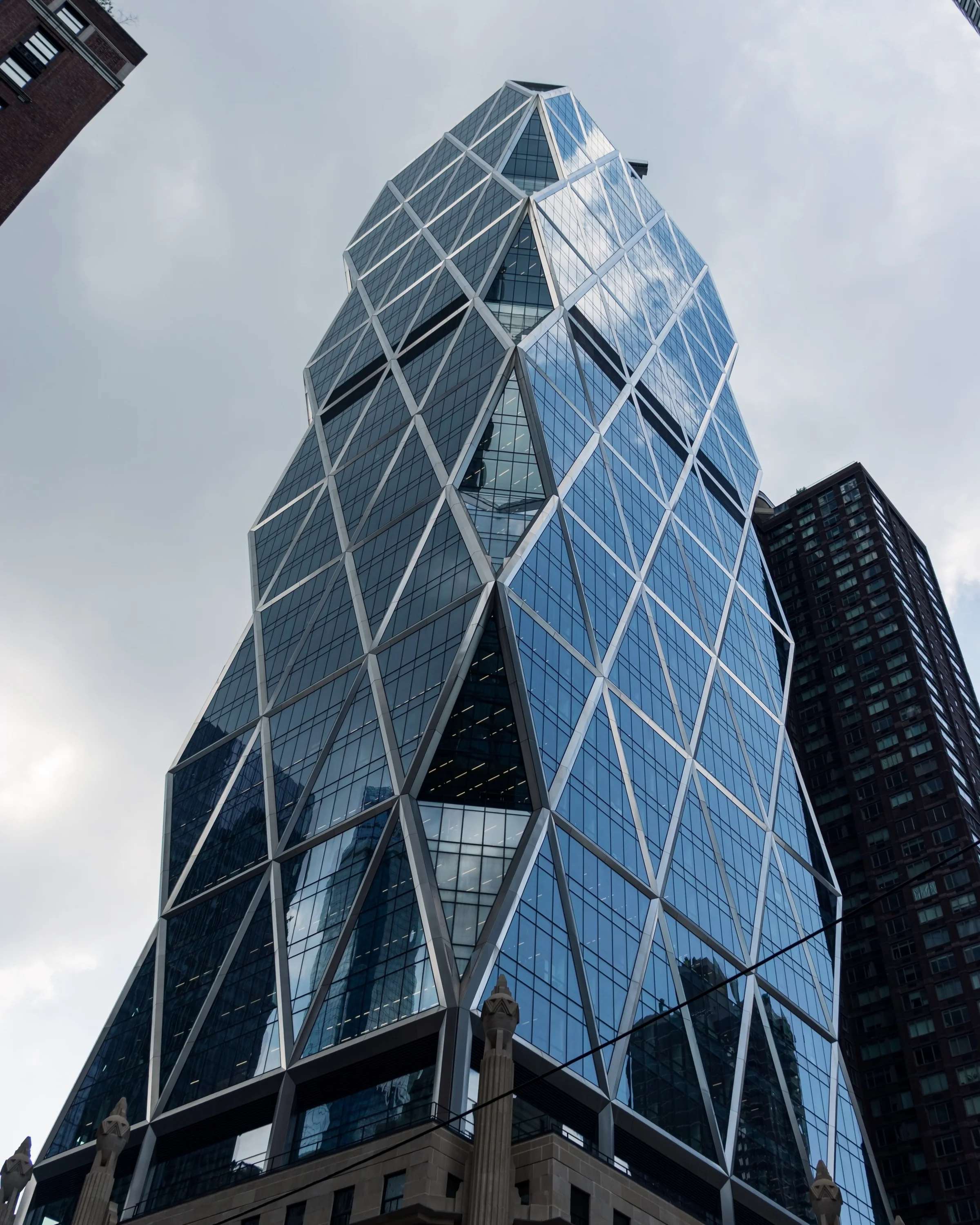 Diagonal structural lines cross the glass facade of a modern tower above an older stone base.