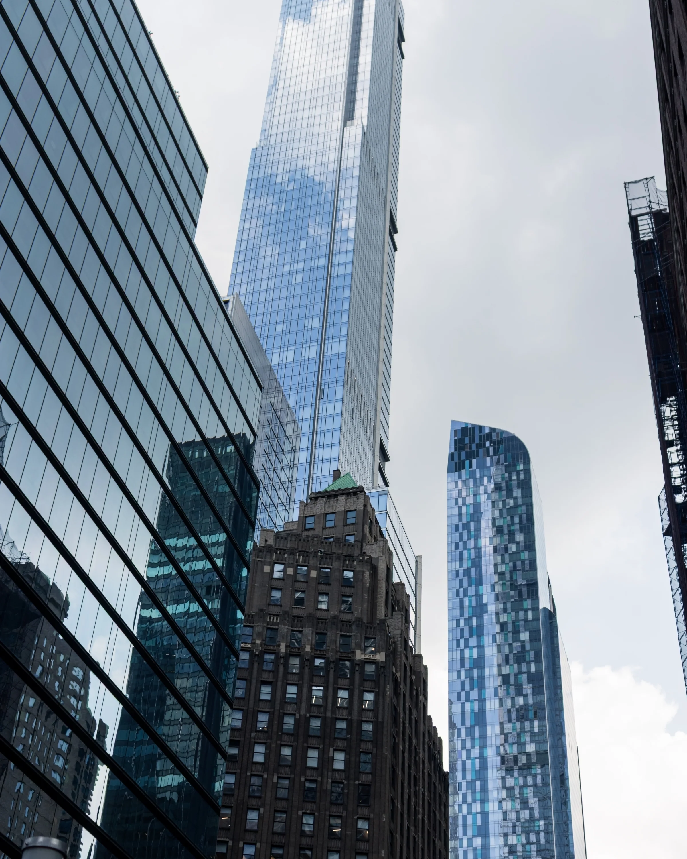 A historic stone building stands below towering glass facades in a dense city street.