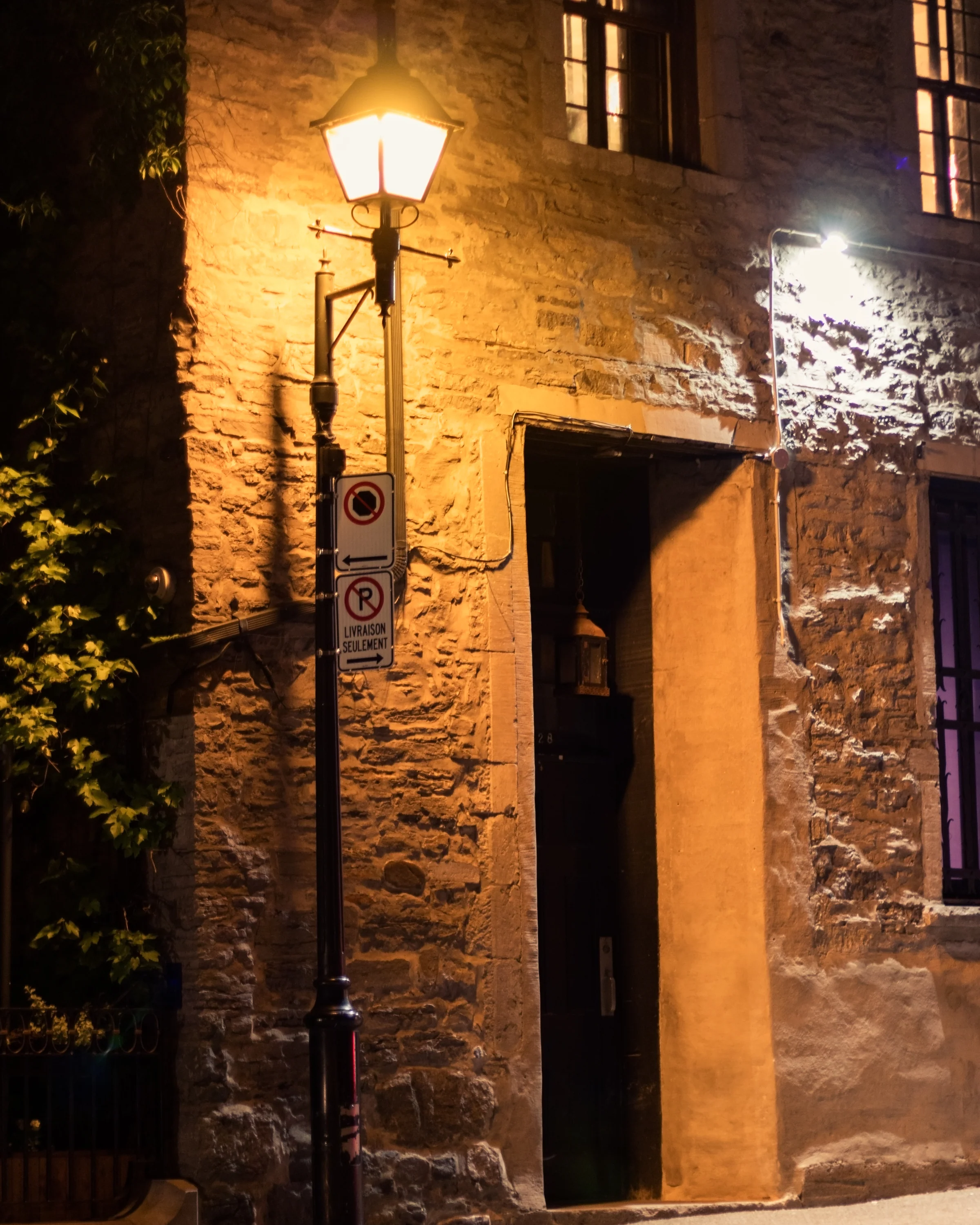 A warm wall lantern illuminates a stone doorway after dark.