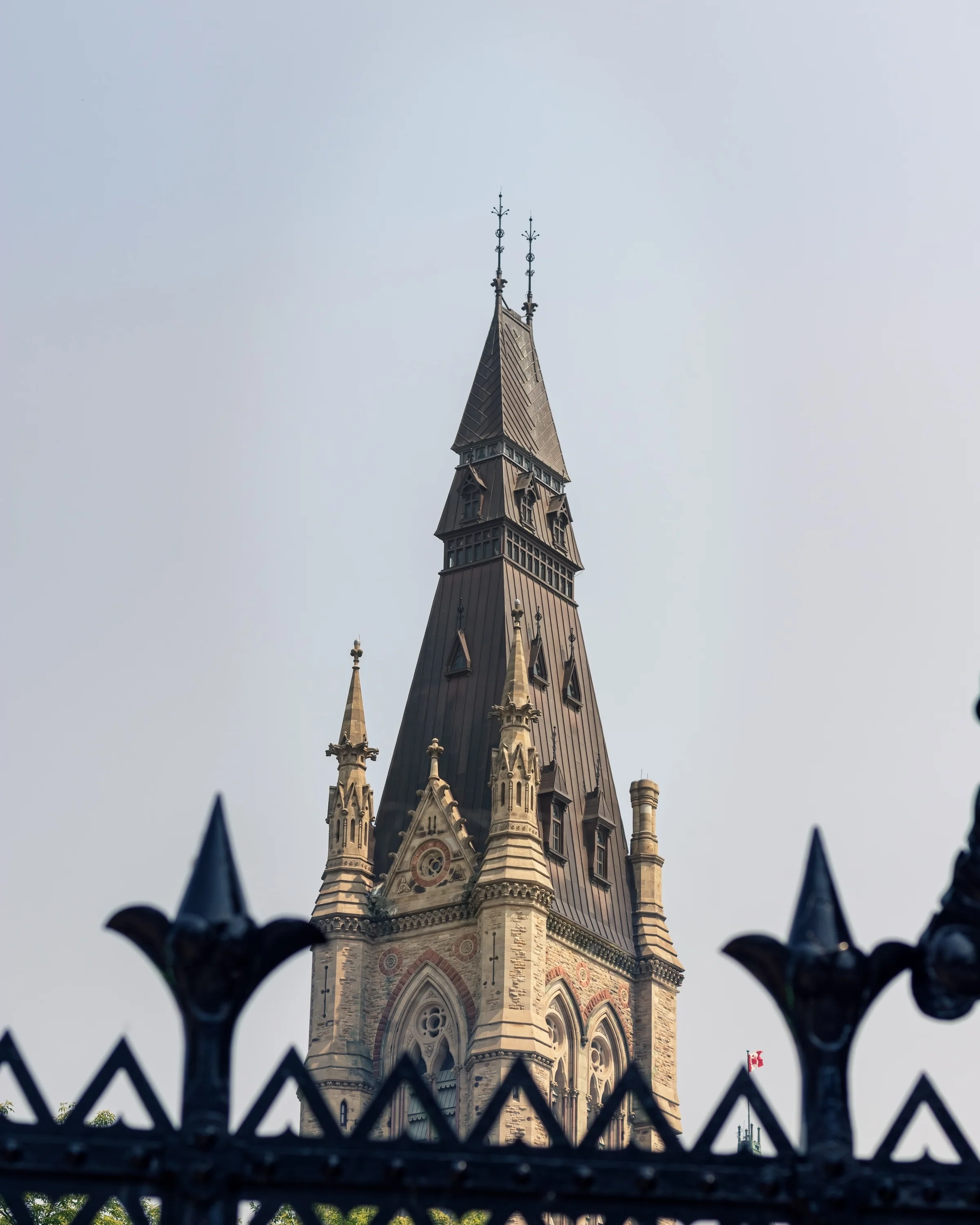 A pointed church spire rises behind the curved silhouette of an iron fence.