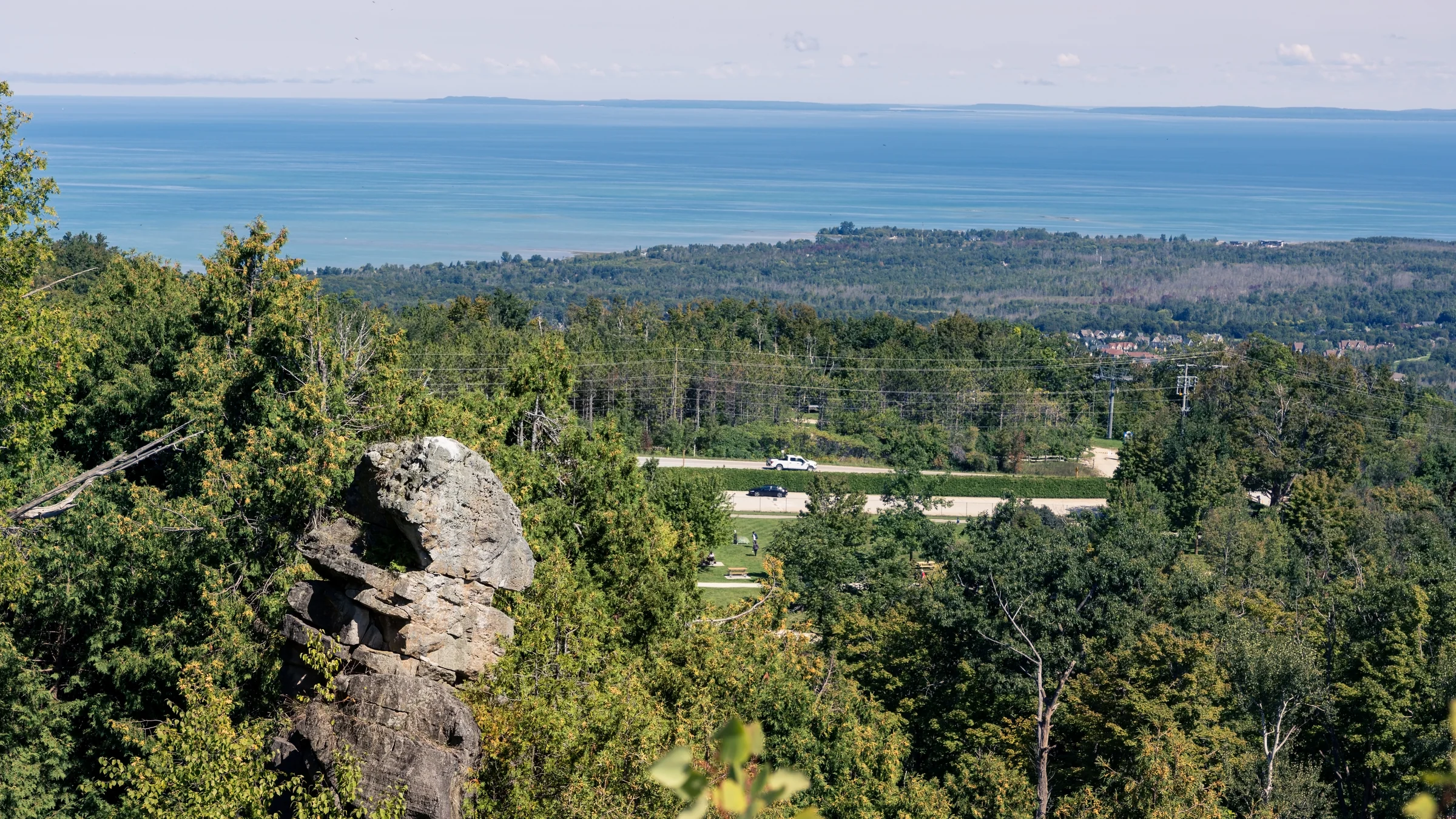 A rocky lookout overlooks green woodland and a broad expanse of blue water.