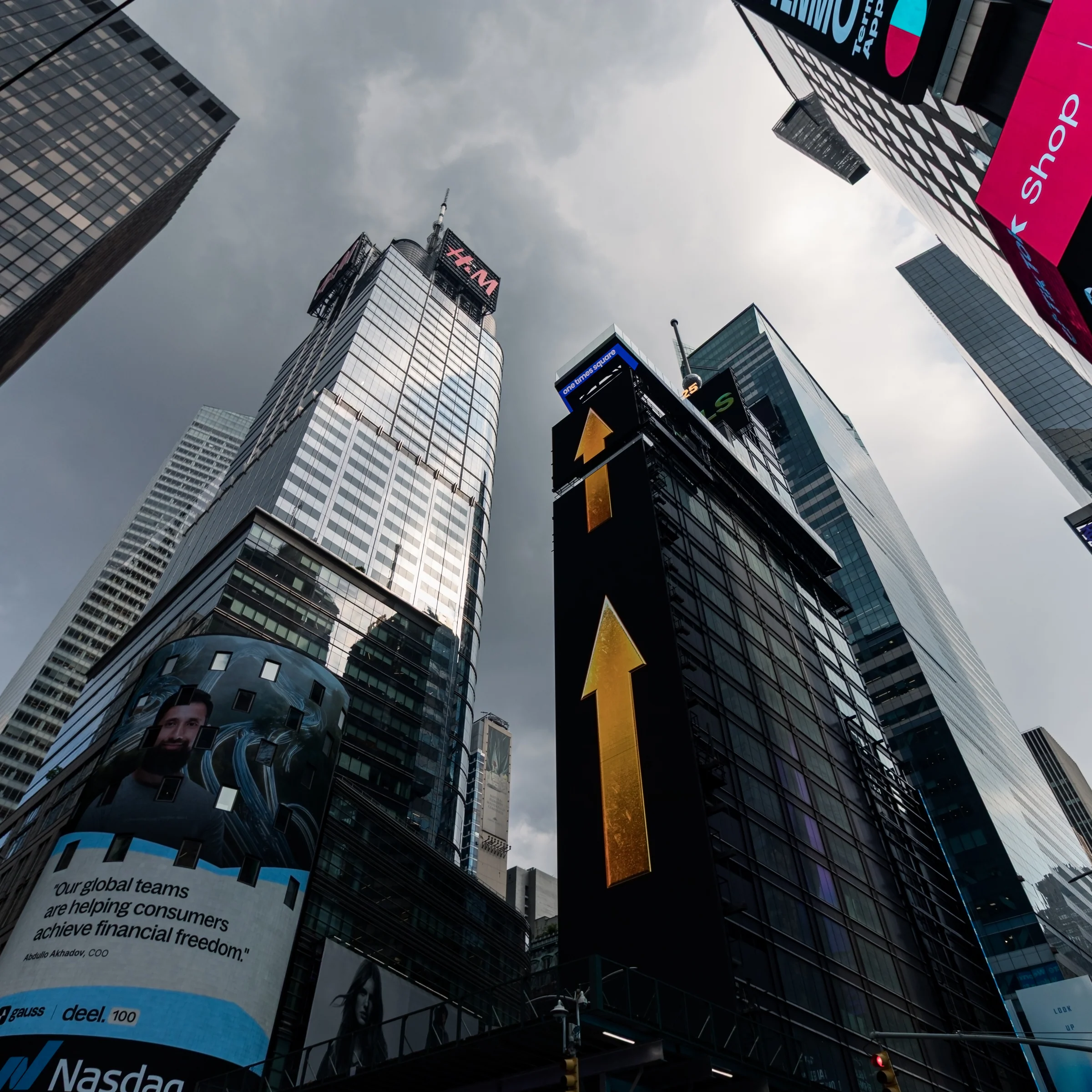 Billboards and tall glass buildings frame a dramatic upward view of the city sky.