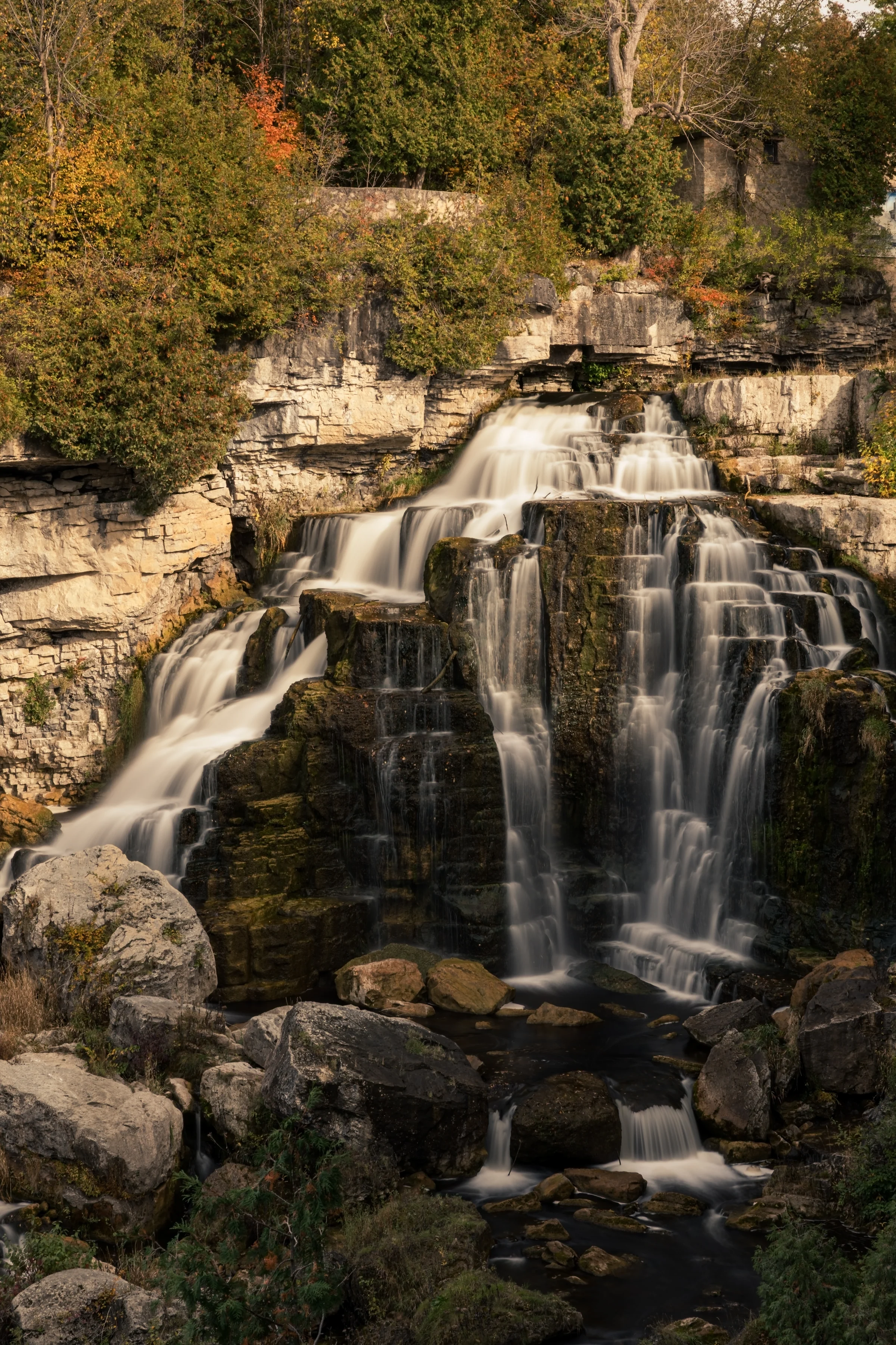 A waterfall drops down a stepped rock face bordered by autumn foliage.