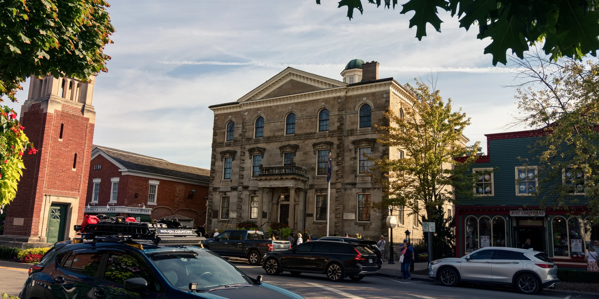 Historic stone buildings line a lively town street beneath a pale blue sky.