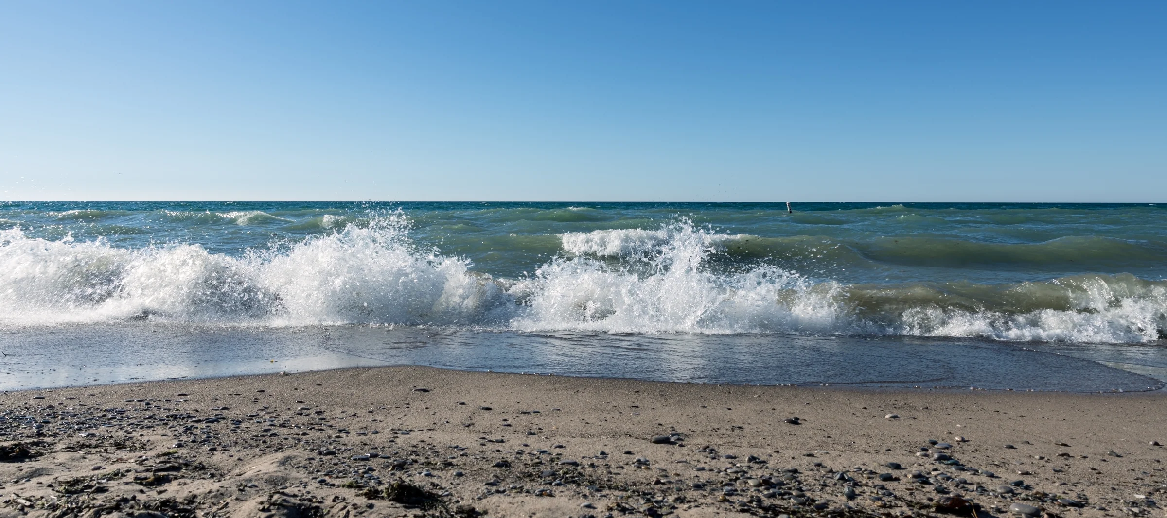 A white-capped wave breaks parallel to a quiet sandy beach.