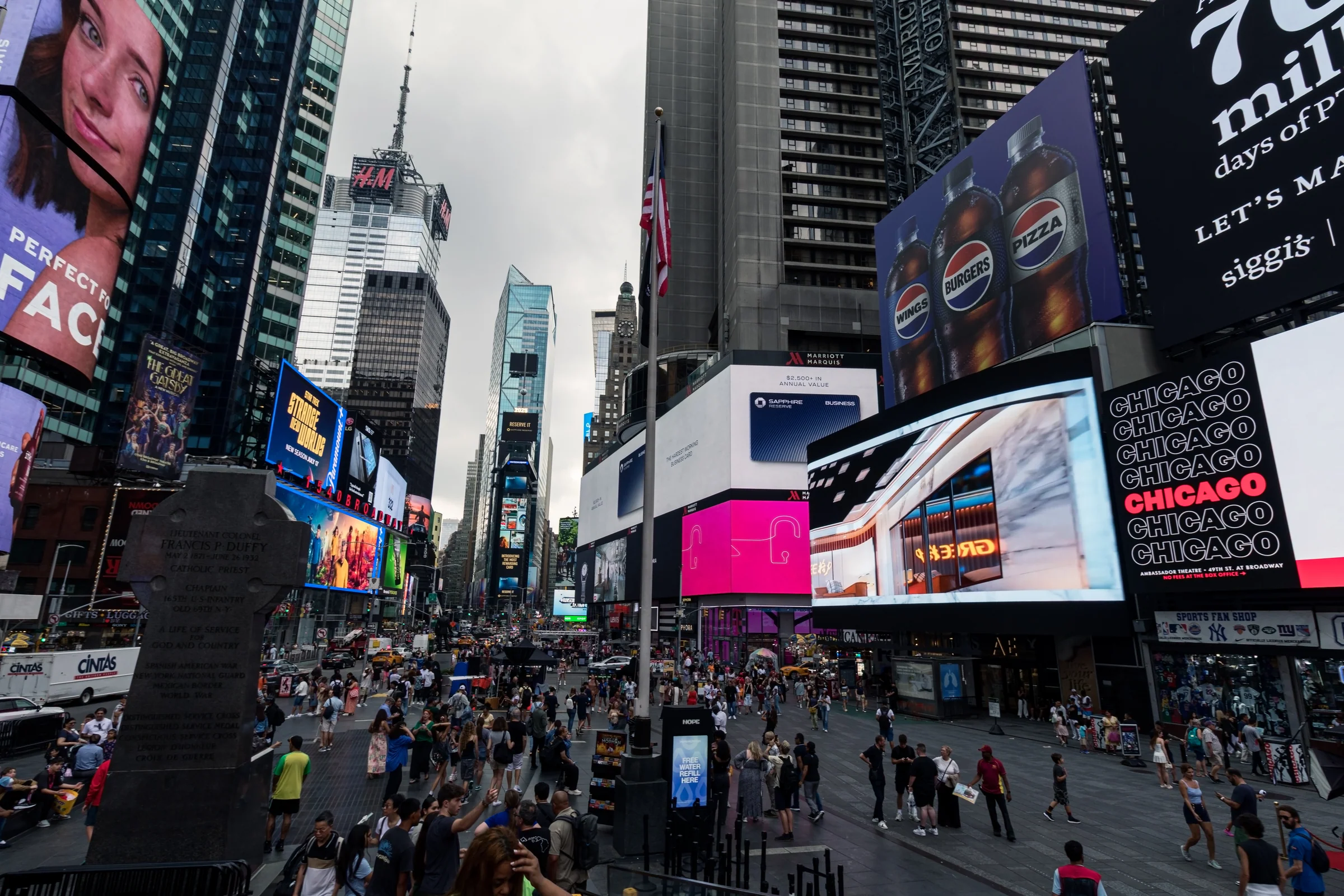 Colourful advertising screens tower over pedestrians gathered in a busy urban square.