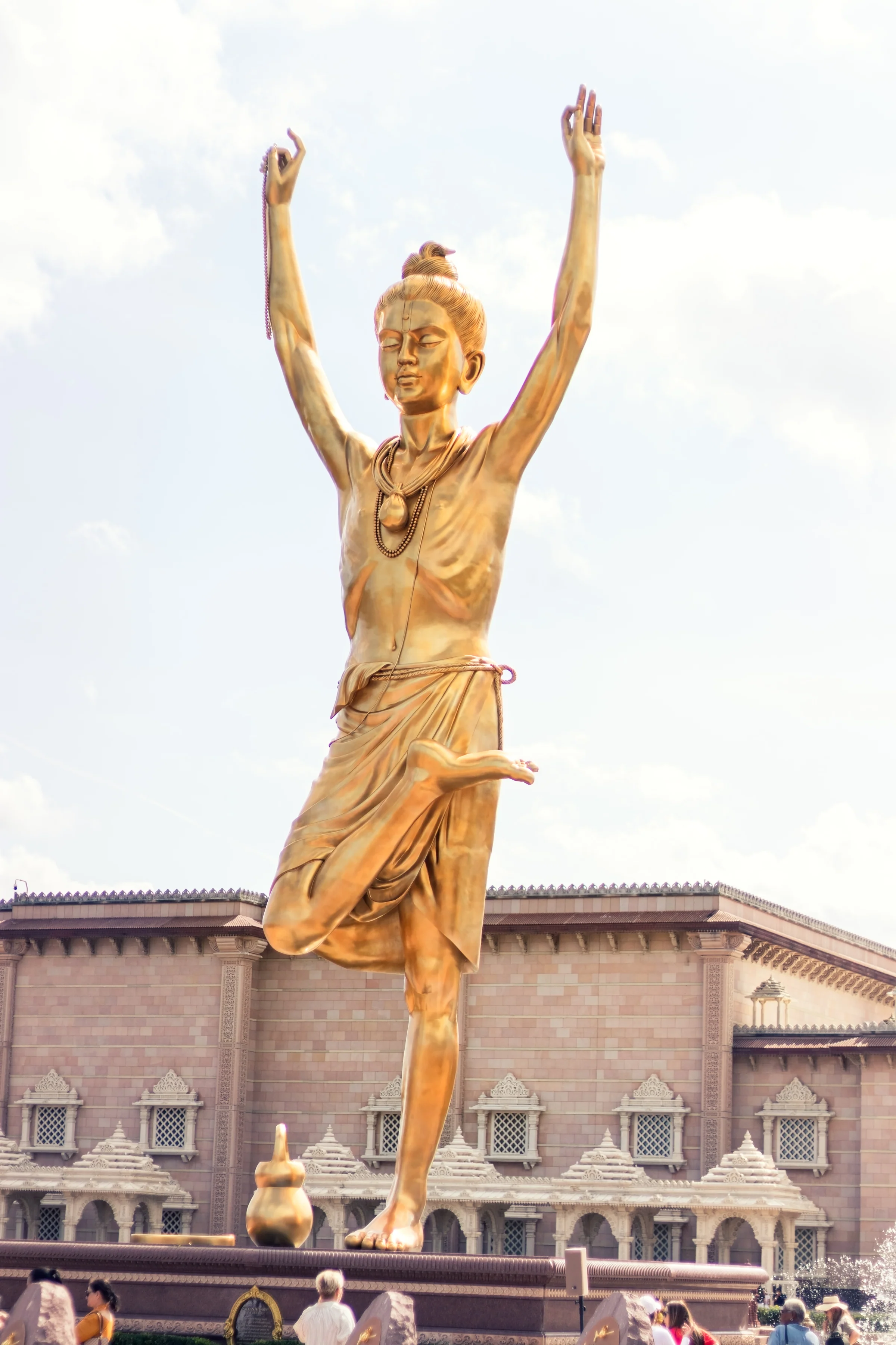 A golden standing statue raises both arms above a busy temple courtyard.