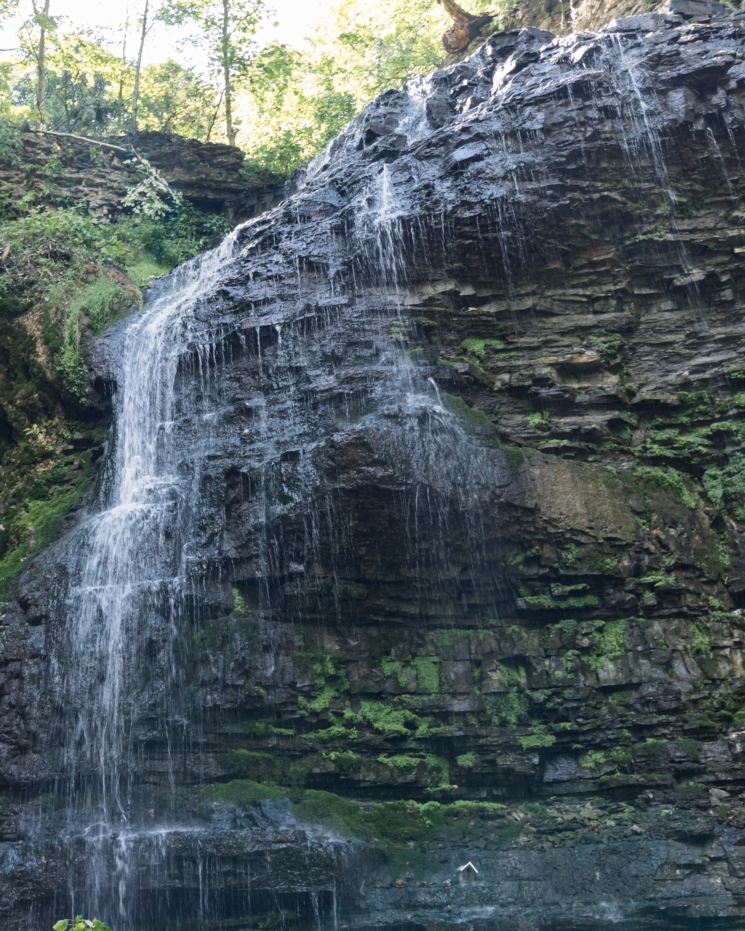 A narrow waterfall spills over a high, dark cliff edged with green vegetation.