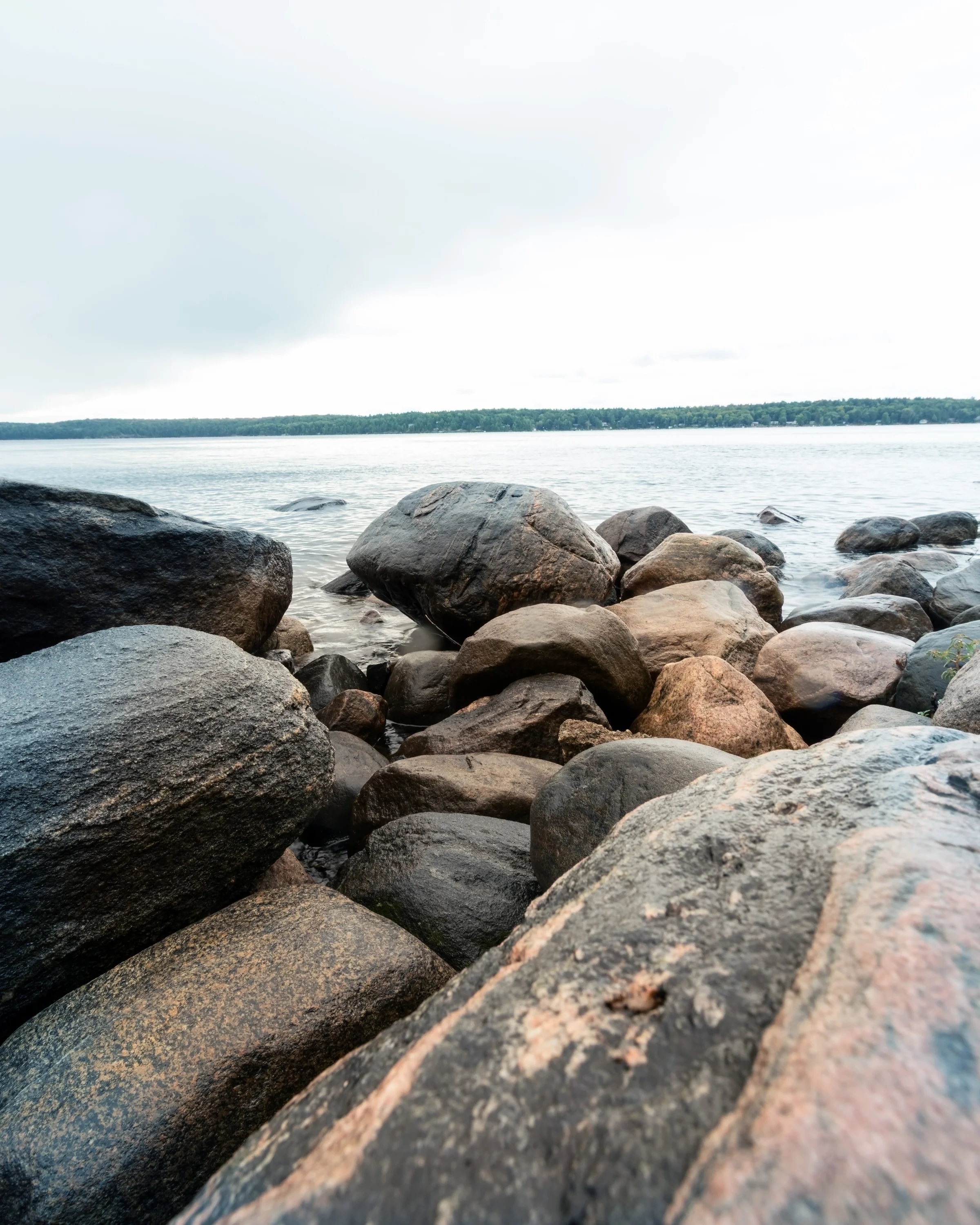 Rounded shoreline boulders lead toward a pale horizon across calm water.