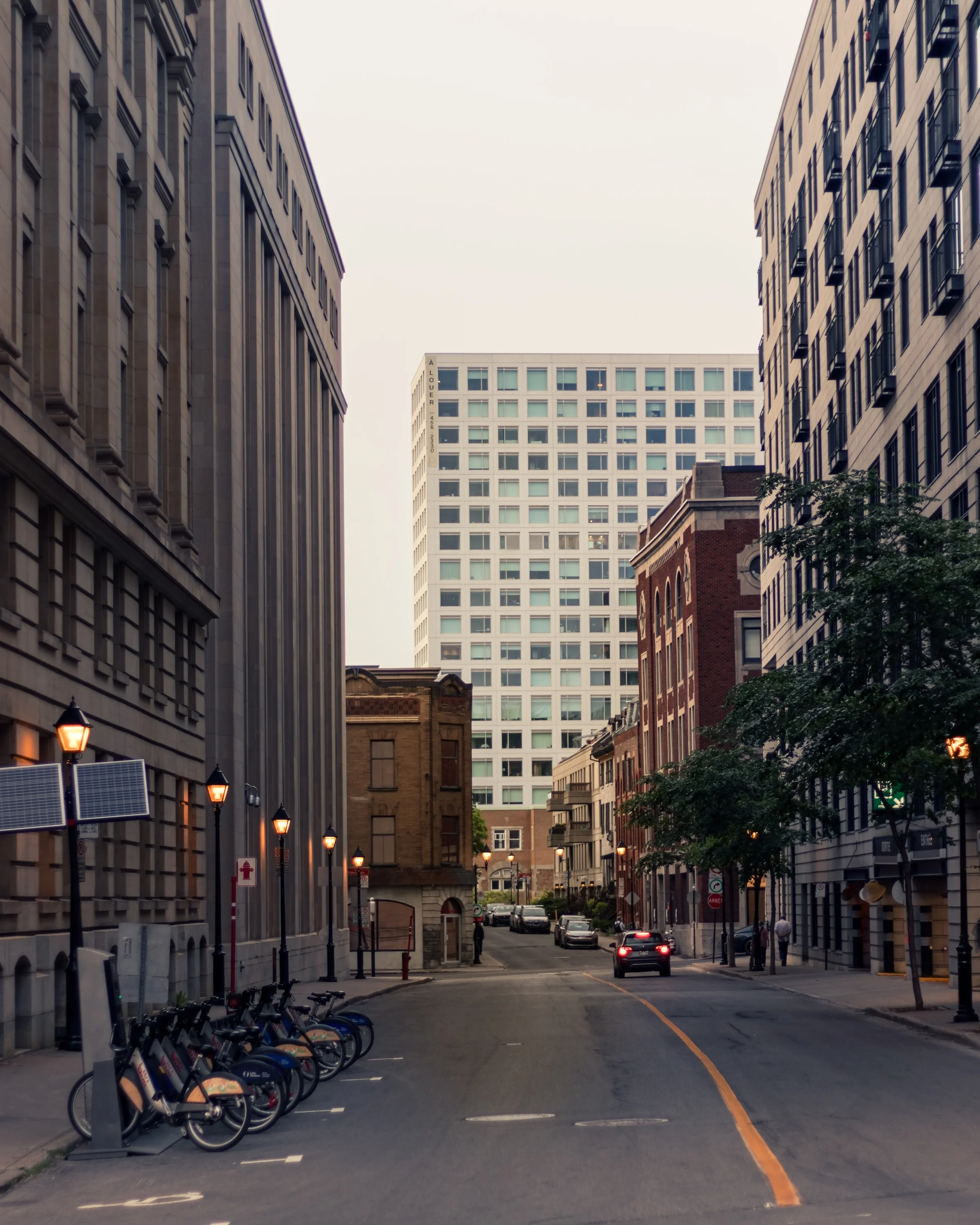 A quiet street recedes between tall urban buildings toward a distant facade.