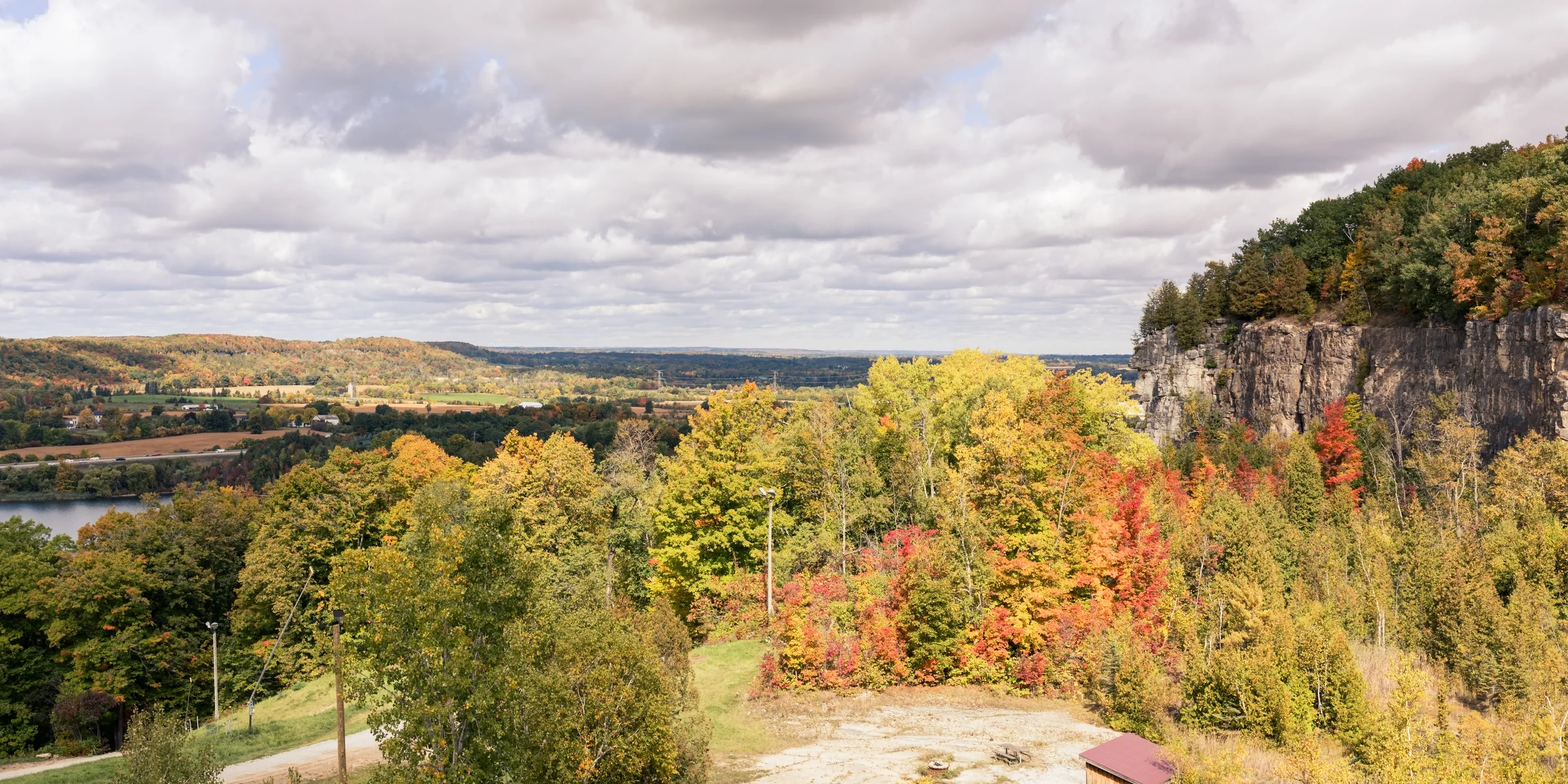 Yellow and orange trees spread beneath a rocky escarpment under a cloud-filled sky.