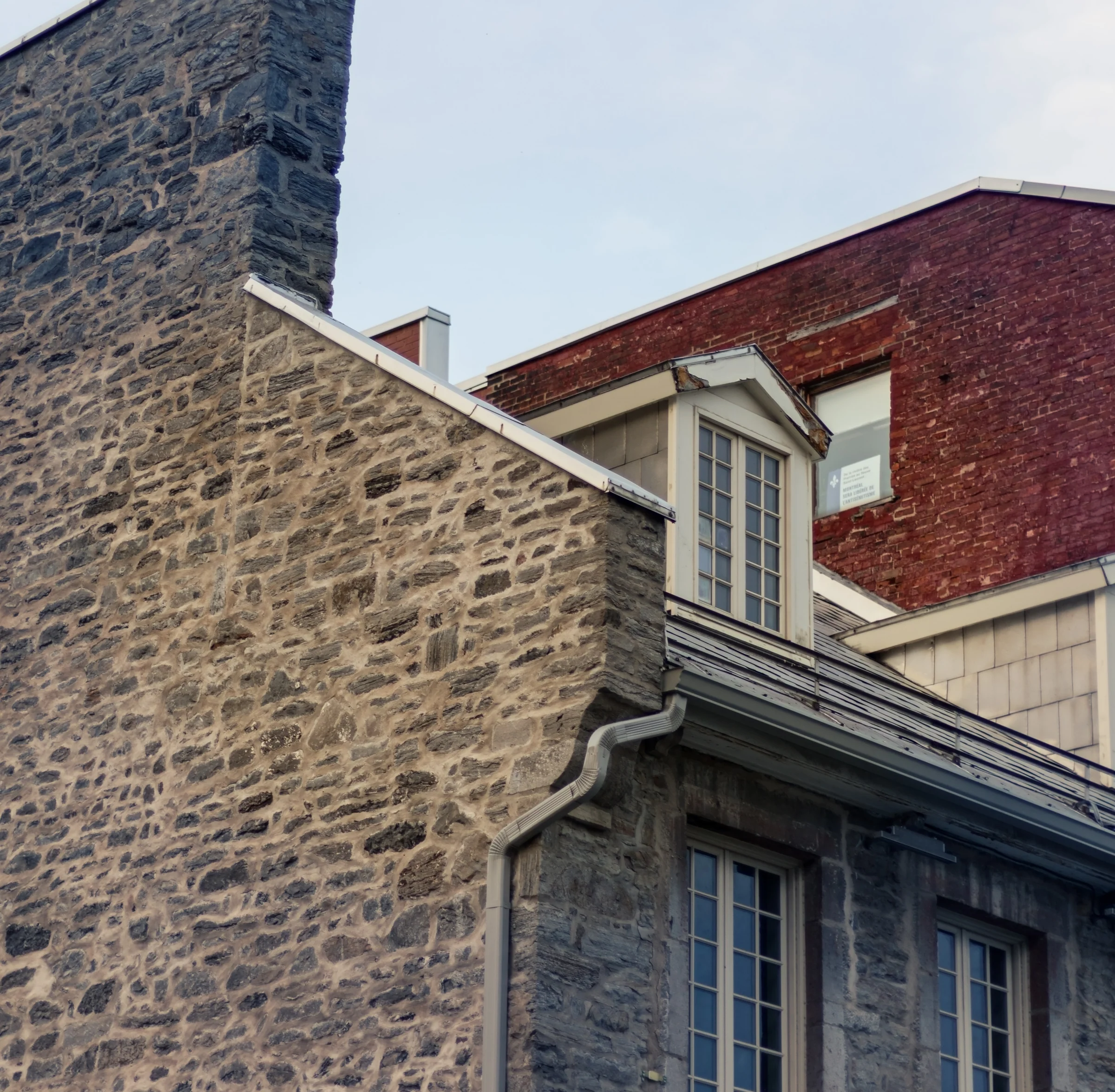 Weathered stone walls, a small dormer, and red brick form a layered architectural detail.