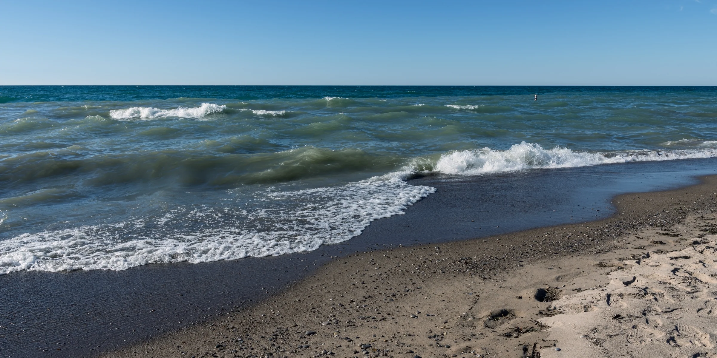 Small waves roll onto a sandy beach beneath a wide, clear blue sky.