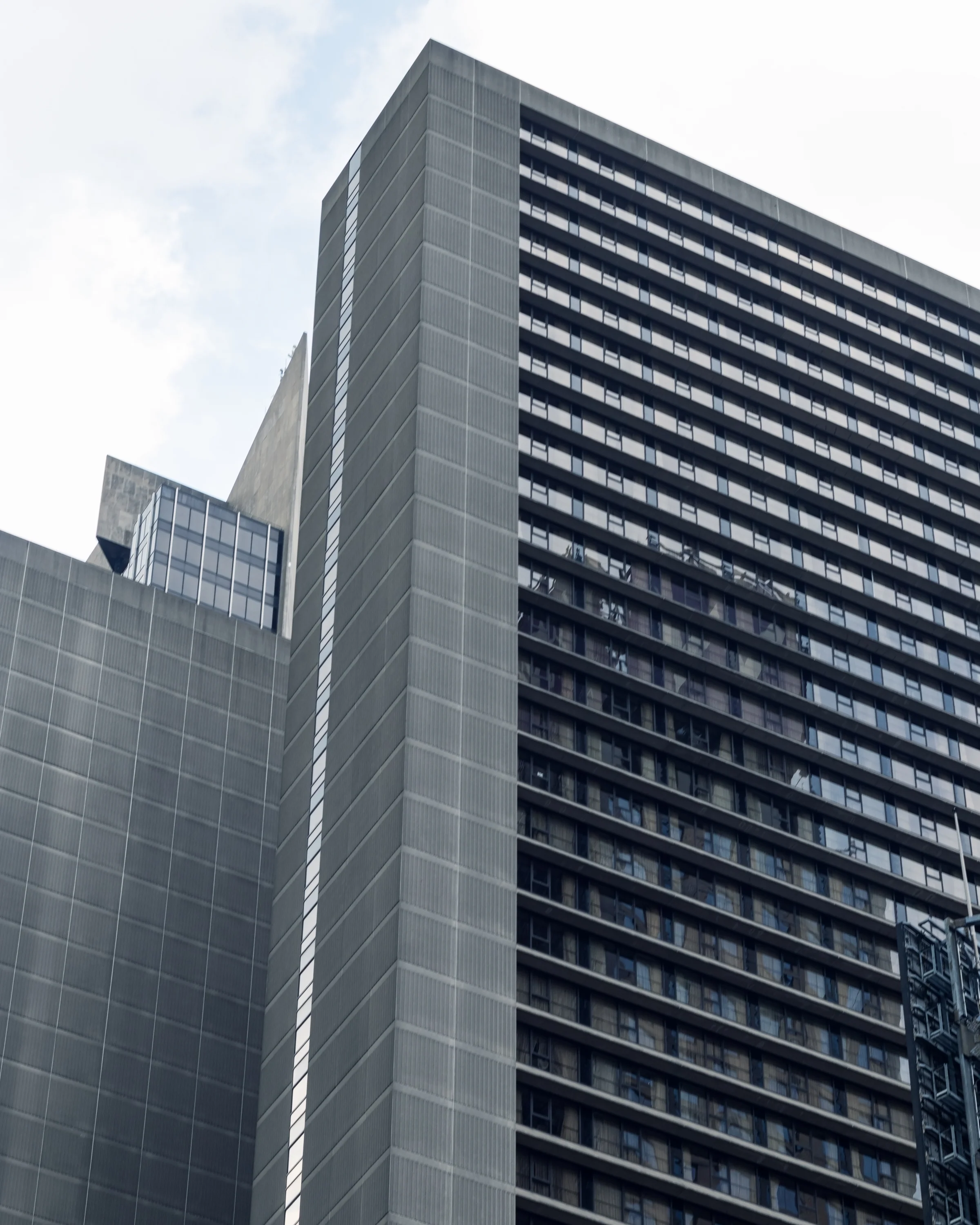 A modern high-rise presents a repeating grid of dark windows and pale horizontal lines.